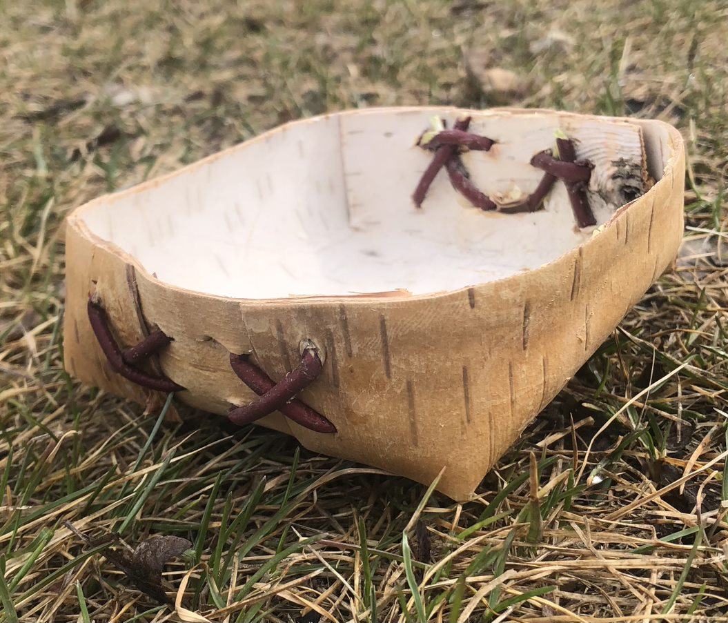 A birchbark basket sits on the grass.