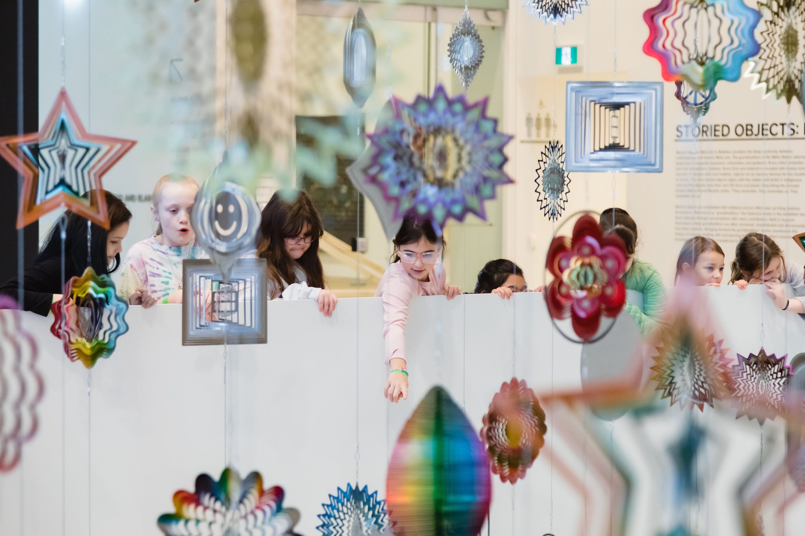 Children look at the work Spinner Forest, made up of thousands of metallic wind spinners in many different shapes.