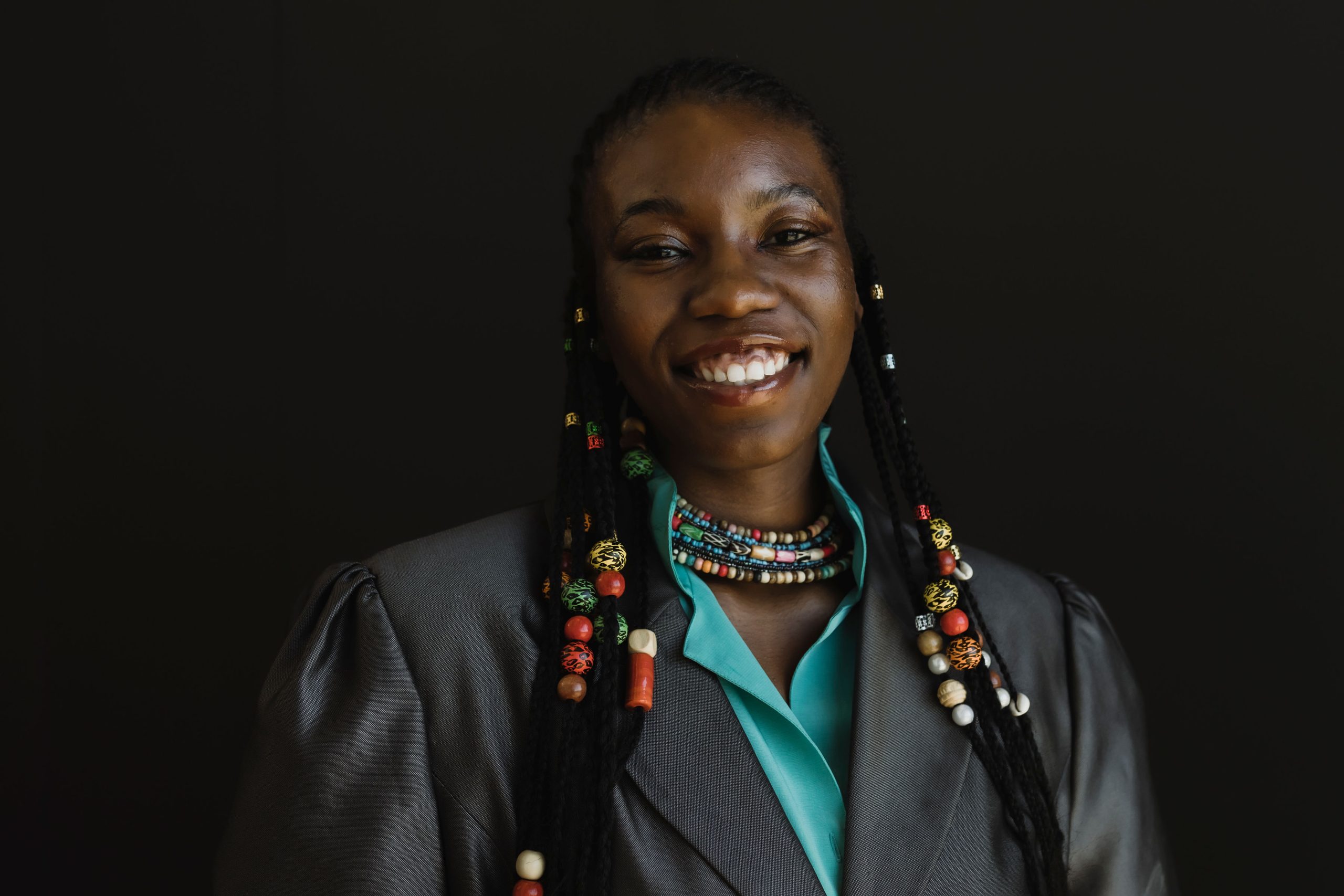 Peace Akintade smiles and stands against a black background.