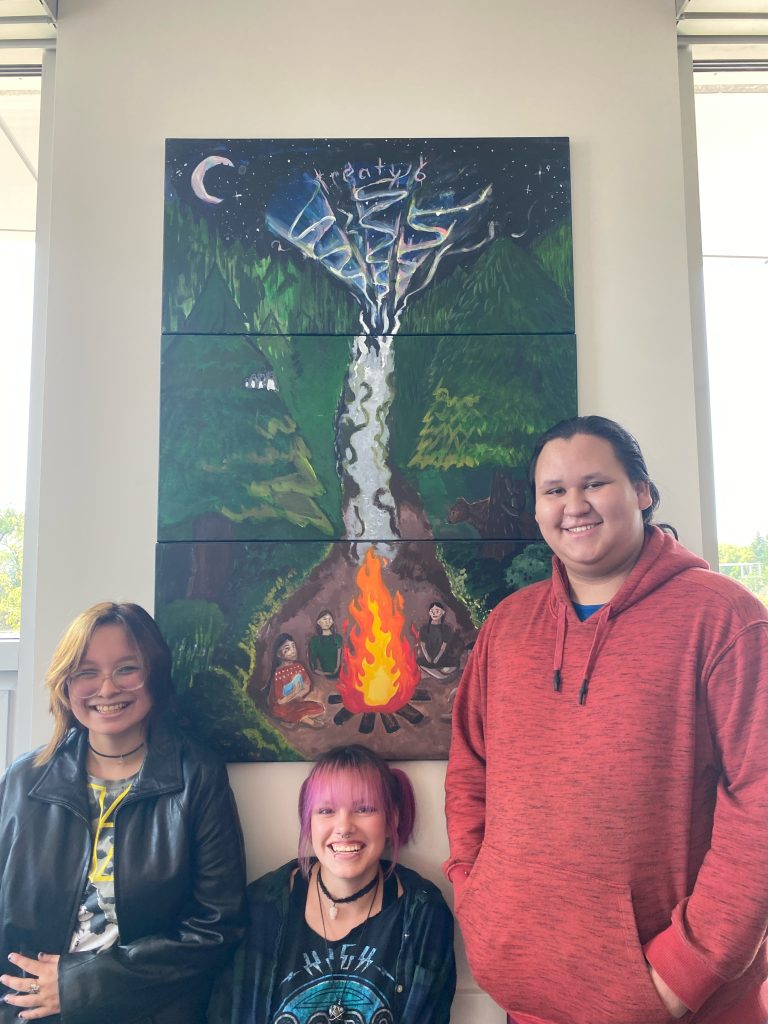 Three high school students pose for a photo in front of a painting they made.