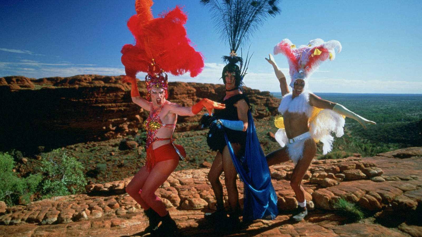 Three people dressed in drag stand near a cliffside.