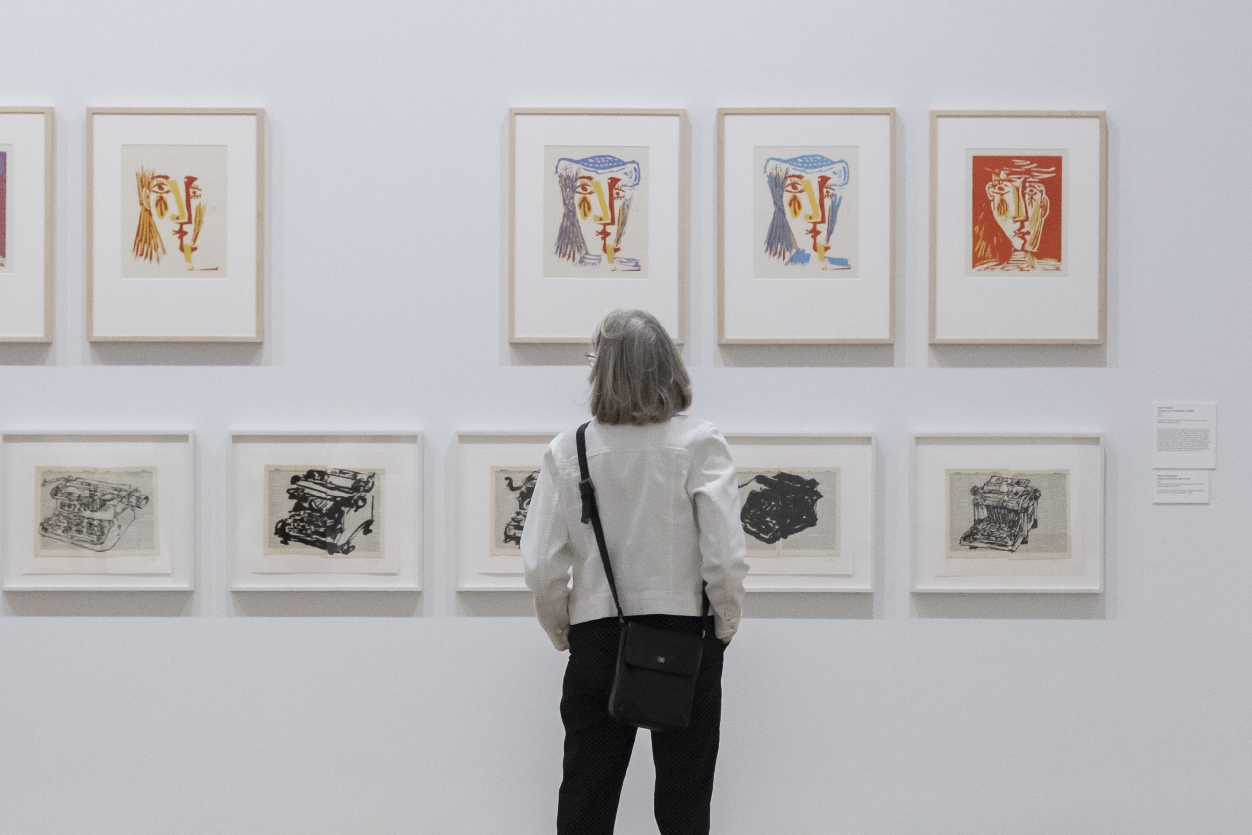 A visitor looks at a gallery wall featuring colourful works by Picasso on the top and black-and-white works by William Kentridge on the bottom.