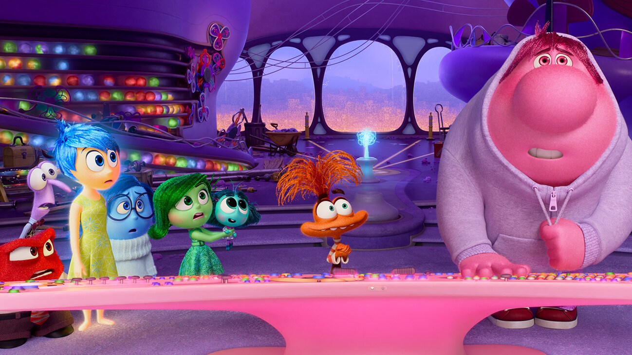 A vibrant and colorful scene featuring animated characters from the movie "Inside Out 2." The characters, representing emotions like Joy, Sadness, Anger, Disgust, and Fear, are gathered around a brightly lit console. Bing Bong, a pink imaginary friend, stands to the right, interacting with the console. The background shows a whimsical and futuristic environment with glowing orbs and vivid colors. The characters appear surprised and focused, suggesting a significant moment in the story.